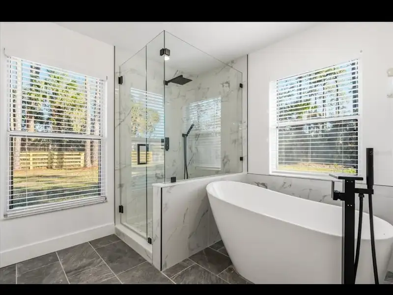 Luxury marble bathroom with glass shower and freestanding tub by JM Home Industries